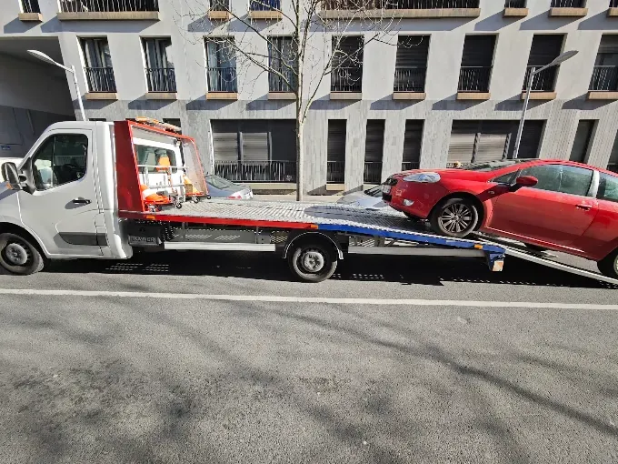 Dépanneuse plateau en train de charger une voiture rouge dans une rue de Paris
