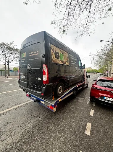 Fourgon utilitaire noir transporté sur un long plateau sur une avenue parisienne